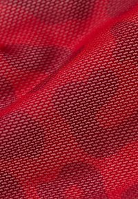 Roter Stoff mit einem strukturierten Muster kleiner geometrischer Formen, das eine subtile und abwechslungsreiche Oberfläche schafft. Das Material wirkt leicht.