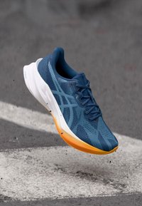 Scarpa da corsa con tomaia in mesh traspirante blu, suola arancione e bianca e sistema di allacciatura, progettata per comfort e prestazioni.