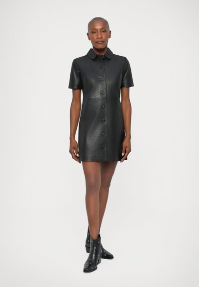 Czarna skórzana sukienka z krótkimi rękawami, zapinana na guziki z kołnierzykiem. Noszona z czarnymi botkami do kostek z elementami metalowymi.