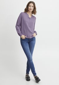 Violeta gara piedurknešu bluze ar V veida kakla izgriezumu un savirknētām aprocēm, apvienota ar ziliem slaidiem džinsiem un melniem platformas mokasīniem ar ķēdes detaļu.