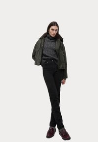 Chaqueta bomber recortada de color verde oliva con cuello marrón, suéter de punto de canalé gris de cuello alto, jeans negros y mocasines burdeos con borlas.