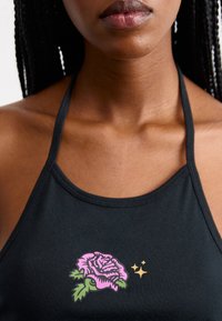 Top a halter nera con un design di rose rosa e verdi e dettagli dorati sul davanti. Realizzato in tessuto morbido ed elasticizzato.