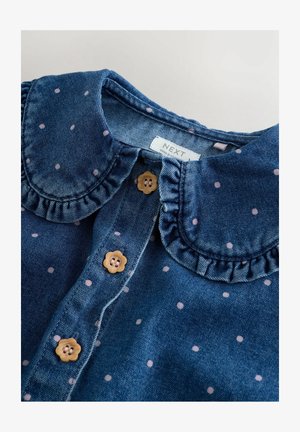 Cămașă din denim cu guler volan, material albastru, buline roz și nasturi florali. Eticheta spune "NEXT."