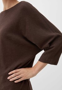 Bruine oversized top met een brede halslijn en driekwartmouwen, gemaakt van een zachte stof met een gladde textuur en subtiele naaddetails.