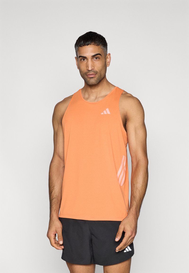 Πορτοκαλί αθλητικό τοπ με στρογγυλή λαιμόκοψη, με λεπτό λογότυπο σε ροζ και πλευρικό διακοσμητικό σχέδιο. Συνδυασμένο με μαύρο σορτς.