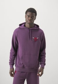 Sudadera morada con bolsillo frontal y puños acanalados. Presenta un logo de toro rojo en el pecho. La tela parece suave y texturizada.