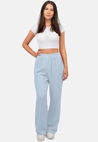 Lichtblauwe, loszittende broek gemaakt van een gestructureerde stof met een elastische tailleband, gecombineerd met een witte cropped top en lichte sneakers.