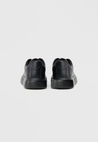 Μαύρα αθλητικά παπούτσια με ανώτερο μέρος από λείο δέρμα, μαξιλαρωμένη σόλα και στρογγυλεμένη μύτη. Διαθέτουν διακριτικό λογότυπο στη φτέρνα και σχεδιασμό με χαμηλή κορυφή.