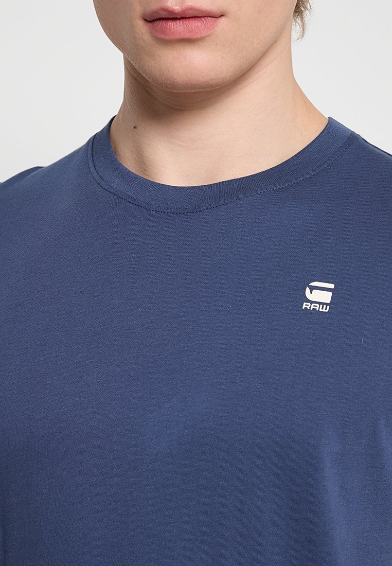 Marineblaue Baumwoll-T-Shirt mit Rundhalsausschnitt, kurzen Ärmeln und einem kleinen weißen Logo auf der Brust. Glatte Textur, lässige Passform.