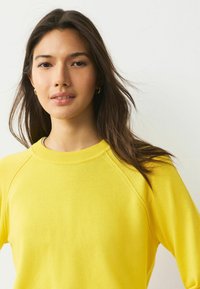 Sárga, puha anyagból készült kerek nyakú pulóver, bordázott nyakkivágással és kényelmes, laza szabással, raglán ujjú dizájnnal a komfort érdekében.