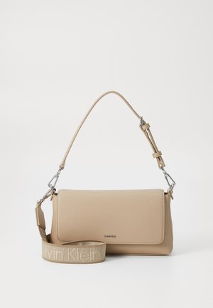 Bolso de mano sintético beige con una textura suave, cierre de solapa en la parte superior y una correa desmontable que presenta "Calvin Klein" en un tono más claro.