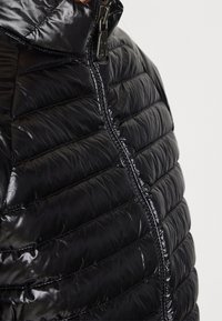 Svart puffer-jacka med ett kviltat mönster, glansig nylonutsida och en framzipper. Har en huva och lågt profilerade sömmar för en elegant look.