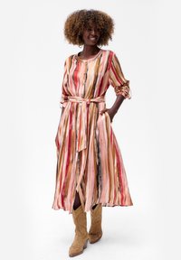 Paski maxidress w pastelowych odcieniach różu, czerwieni i brązu z guzikami z przodu, paskiem w talii i podwiniętymi rękawami. Noszony z jasnobrązowymi kowbojkami.