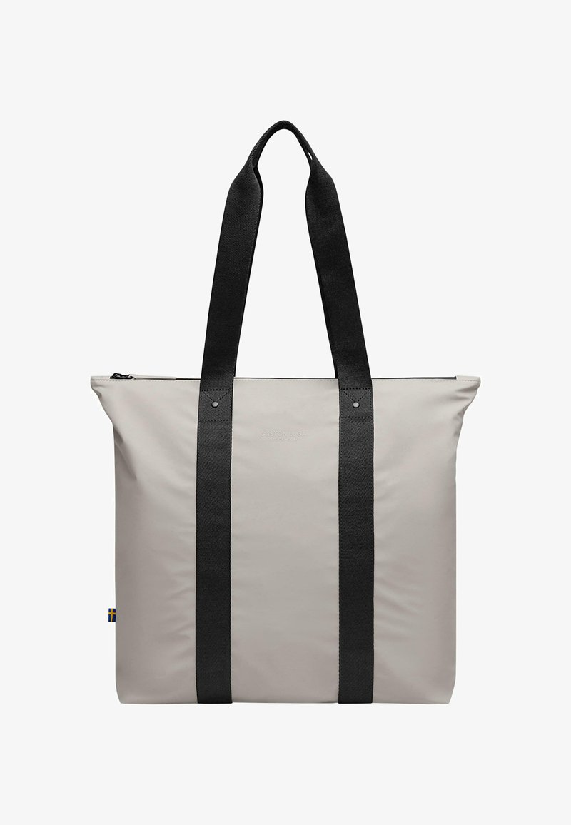Sac tote gris avec des poignées noires, présentant une texture lisse et mate. Comprend une fermeture éclair et une empreinte de logo à l'avant.