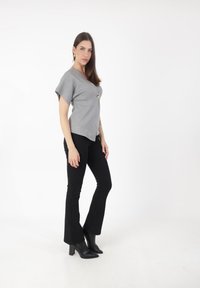 Top gris de manga corta con escote en V y botón dorado en acento, combinado con pantalones negros de campana y botas negras de tacón a la altura del tobillo.