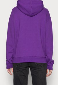 Felpa con cappuccio viola dal fit rilassato, con polsini e orlo ribattuti, texture morbida e un design semplice. Indossata con pantaloni di jeans neri.