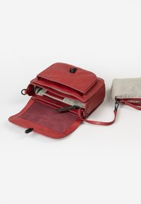 Rode leren tas met een omslagflap, ritscompartimenten en een gestreepte stoffen zak. Zachte textuur en ronde vorm, met metalen accenten.