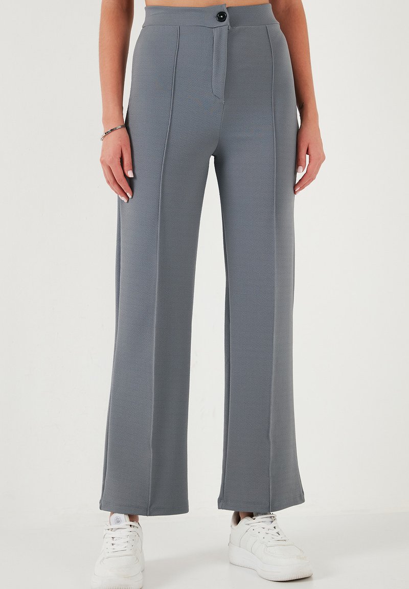 Gray wide-leg trousers made of textured fabric, featuring a front button closure and stitched panel details, paired with white sneakers.