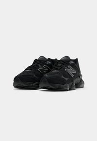 Baskets de sport noires avec des panneaux en mesh, bout arrondi, semelle amortissante et logo 'N' en gris sur les côtés.