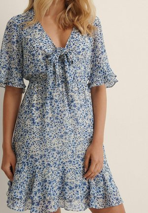 Robe fleurie bleu clair et blanc. Manches courtes à bords volantés, taille cintrée avec un lien au niveau de l'encolure. Ourlet évasé.