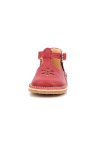 Zapato de piel roja con diseño de flor recortada en la puntera, correa ajustable con hebilla de metal y suela de goma marrón. Textura suave, talón cerrado.