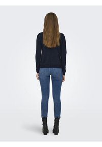 Pull bleu marine à manches longues, coupe ajustée, et ourlet côtelé, associé à un jean skinny bleu foncé et des bottines noires.
