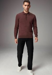 Suéter de punto color burdeos con cuello con solapa y tres botones, combinado con jeans negros y zapatillas blancas sobre un fondo neutro.