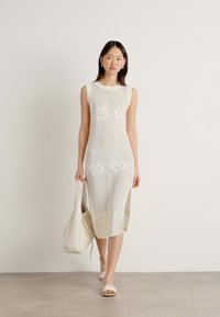 Knit midi dress in off-white featuring a fitted design, floral patterns, side slits, and a ribbed texture; paired with a cream handbag.