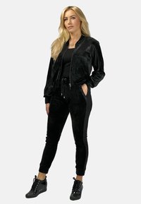 Czarny welurowy dres z krótką bomberką, elastyczną talią i bocznymi kieszeniami; zestawiony z czarnymi sneakersami z wiązaniem.