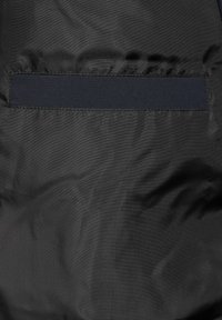 Czarna tkanina ma gładką fakturę z poziomym paskiem kontrastowego materiału blisko górnej części. Nie widać wzorów ani metalicznych detali.