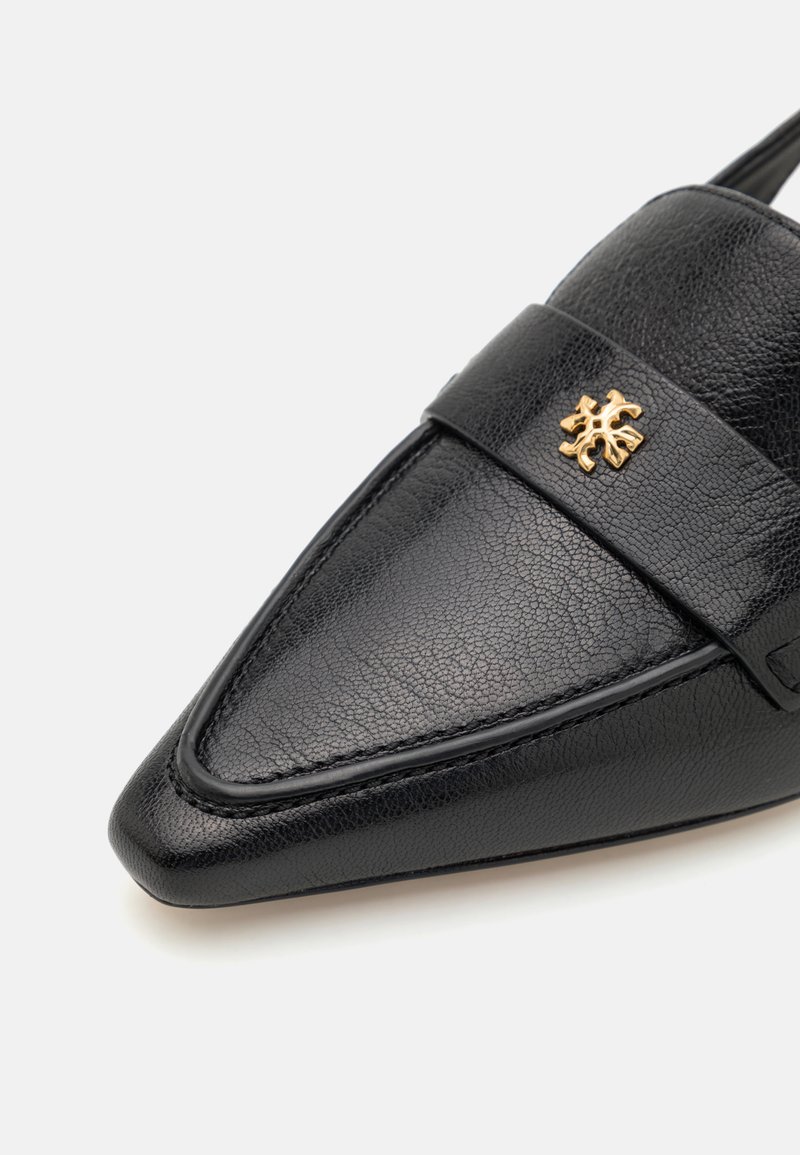 Loafer noir en cuir pointu avec une finition texturée et un emblème ornemental en or sur la sangle en haut.