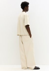 Tricou oversized bej cu mâneci scurte și pantaloni bej cu croi lejer, având două buzunare la spate. Purtați cu sandale negre cu bretele.