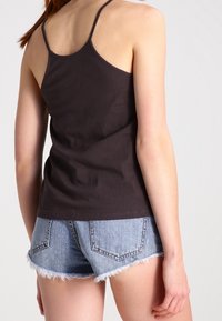 Top de tirantes finos de algodón negro, combinado con pantalones cortos de mezclilla azul claro con bajos deshilachados y bolsillos traseros.