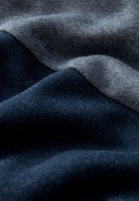 Tissu doux plié montrant deux nuances de bleu, avec une texture tricotée lisse et des ombres délicates soulignant le matériau drapé.