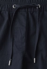 Navyblaue Jogginghose mit elastischem Bund, ausgestattet mit einer Kordel und silbernen Metallspitzen, sichtbaren Nähdetails und einer Tasche.
