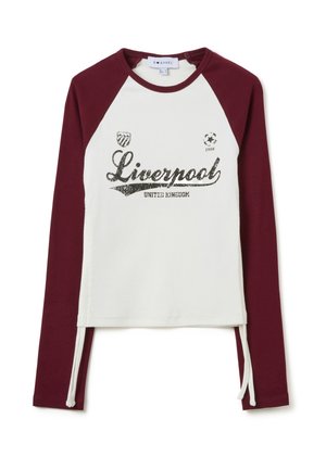Camisa de manga larga con cuerpo blanco y mangas raglán burdeos. Presenta un gráfico de "Liverpool" con lentejuelas y cordones en los laterales.