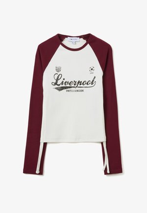Camisa de manga larga con cuerpo blanco y mangas raglán burdeos. Presenta un gráfico de "Liverpool" con lentejuelas y cordones en los laterales.