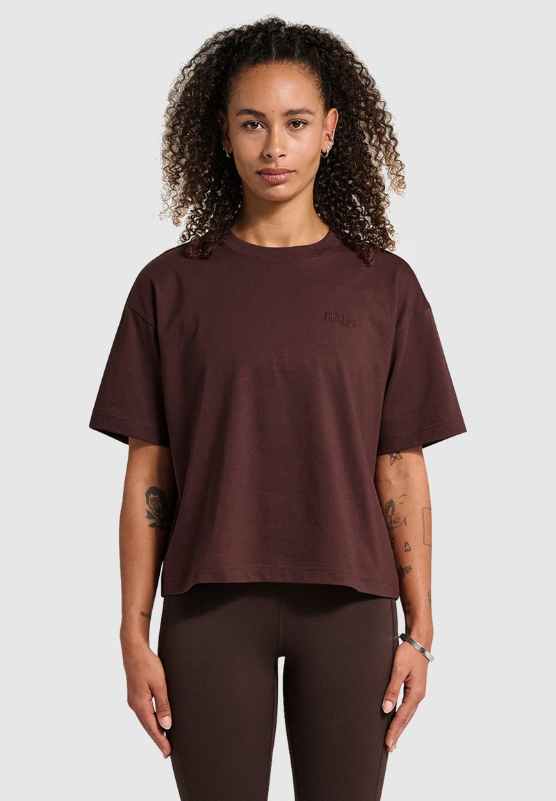 Bordeaux katoenen t-shirt met een relaxed fit, korte mouwen en een ronde hals. Gekenmerkt door een geborduurd logo op de borst. In combinatie met bruine leggings.