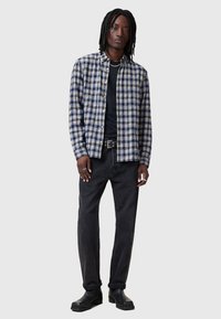Geruite flanellen shirt in blauw, beige en wit over een zwart t-shirt. Ggedragen met zwarte jeans en leren laarzen, geaccentueerd met een riem.