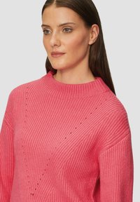Rosa gestrickter Pullover mit geripptem Textur, hohem Kragen und diagonalen Musterakzenten auf der Brust und den Schultern.