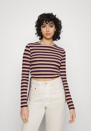 Top cropped de manga longa às riscas em bordeaux e creme, com textura canelada e decote branco, combinado com calças de cintura alta de cor clara.
