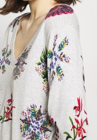 Gray v-neck sweater with floral embroidery in vibrant colors, featuring various plants and flowers on shoulders and sleeves. Soft texture.