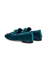 Mocasines de terciopelo verde azulado con suela plana negra, adornados con tachuelas doradas y detalles decorativos en la parte superior. Diseño de punta redonda.