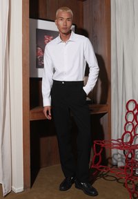 Witte lange mouwen shirt met een kraag, gecombineerd met zwarte broek. De outfit heeft een eenvoudige knoopdetail en wordt aangevuld met zwarte schoenen.