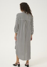 Striped long shirt dress in cream and navy, with 3/4 sleeves, a buttoned collar, and a high-low hemline, featuring a pleat detail at the back.