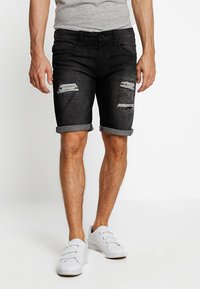 Pantaloni corti in denim neri con risvolti e dettagli strappati; design a cinque tasche; abbinati a sneaker bianche.