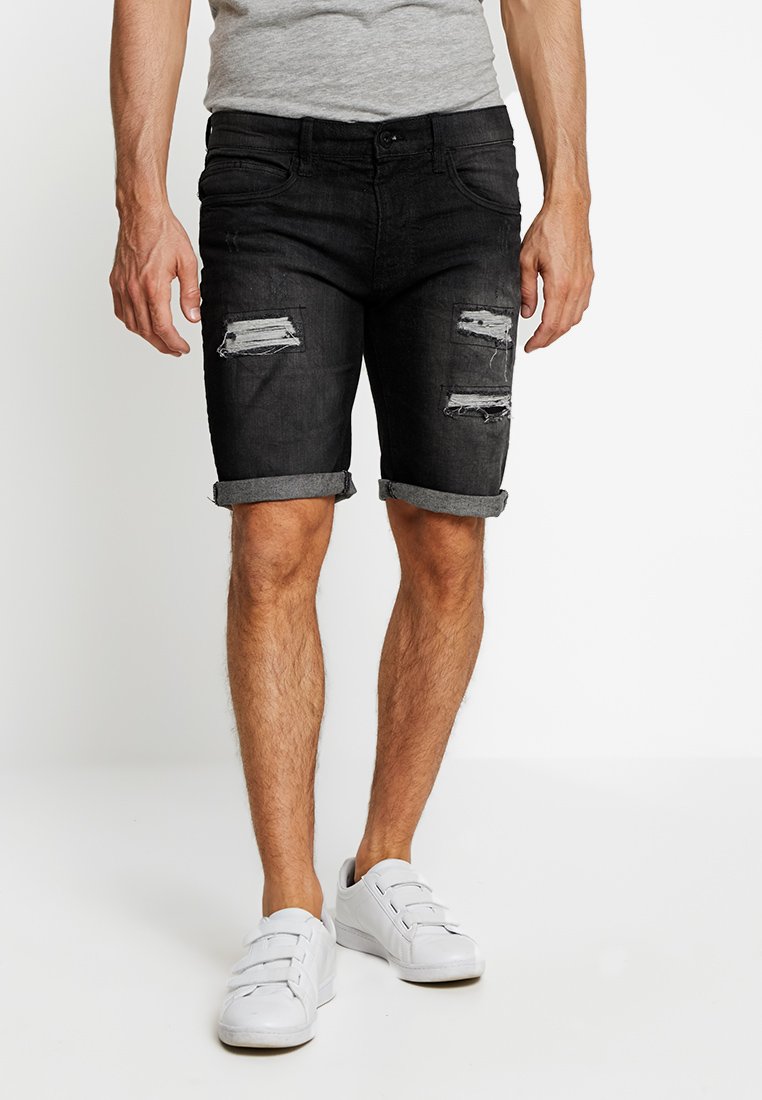 Pantaloni corti in denim neri con risvolti e dettagli strappati; design a cinque tasche; abbinati a sneaker bianche.