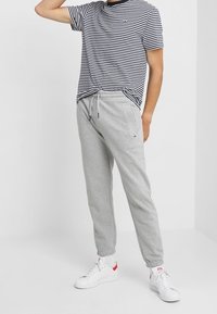 Šedé tepláky s elastickými manžetami, spárované s námořnickou modrou a bílou pruhovanou košilí s krátkým rukávem. Bílé tenisky s červenými akcenty.