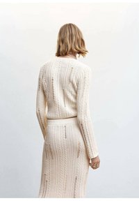 Strickpullover- und Rockset in Creme, mit vertikalen Rippungen und kleinen Ausschnitten, im taillierten Design mit langen Ärmeln.