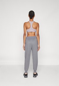 Top de desporto em lilás claro com costas abertas e calças de jogging cinzas. As calças possuem punhos ajustados, criando um ajuste relaxado para conforto.